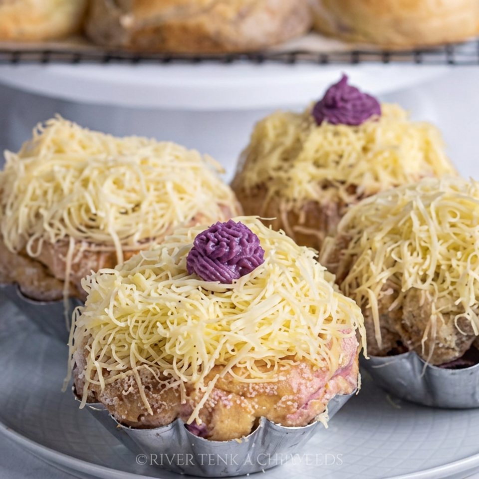 Four golden pastries topped with shredded cheese and purple frosting sit in individual tins on a gray plate.