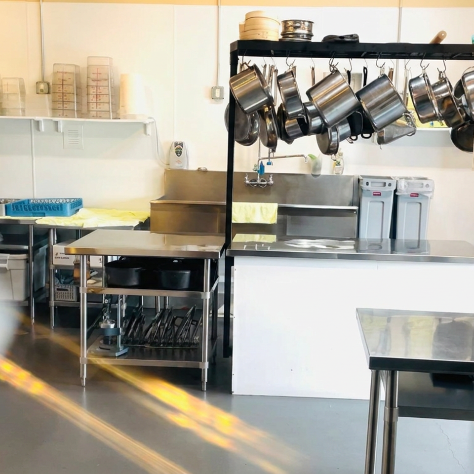 Restaurant kitchen prep area with stainless-steel counters, hanging pots, bamboo steamers, mixers, and organized cooking equipment.